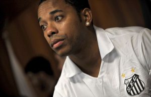 Robinho Begins 9-Year Brazil Rape Sentence Robinho in prison uniform walks between guards inside a Brazilian jail corridor.