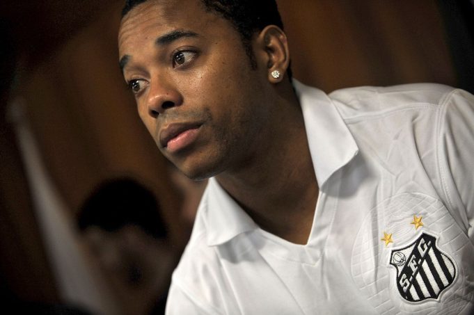 Robinho Brazil Prison 2024 Robinho in prison uniform walks between guards inside a Brazilian jail corridor.